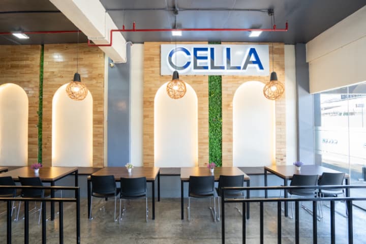 CELLA語学学校の学生ラウンジエリア。木目とグリーンを取り入れたモダンな内装で、壁面にはCELLAのロゴサインが設置されている。学習や休憩にも適した落ち着いたスペース