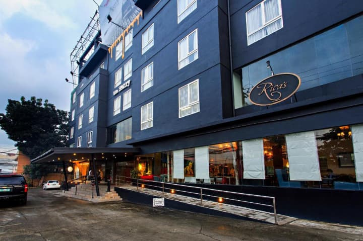 CELLAプレミアムキャンパスの外観写真。もともとヘンリーホテルとして使われていた建物で、黒を基調としたモダンな外観と、1階にはカフェレストラン『Rica's』の看板が見える。ホテル仕様の快適な学習環境が特徴