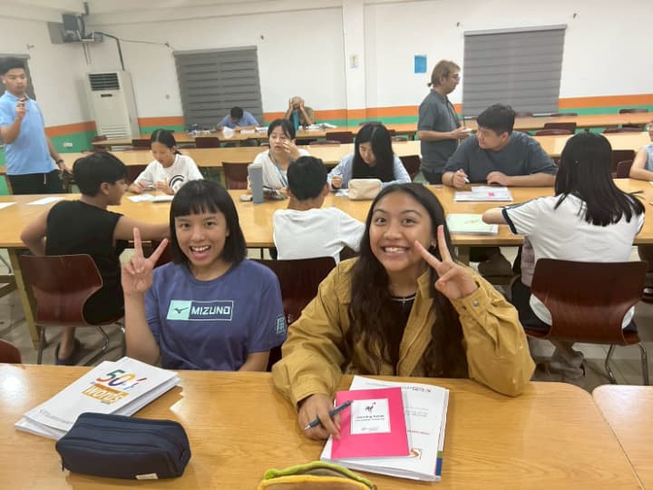 Global Standardの夜間クラスで勉強する生徒たち。手前の2人の女性がピースサイン。