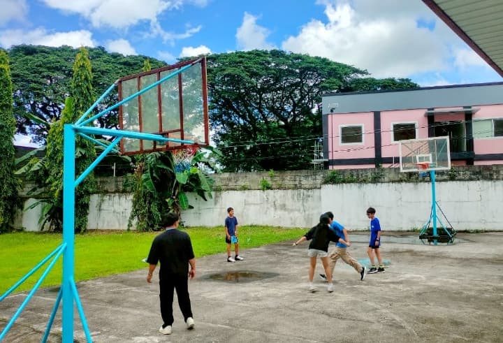子供たちが屋外のコートでバスケットボールをしている様子。