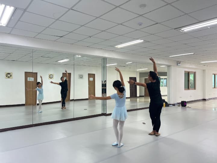 バレエスタジオで、インストラクターが鏡の前で少女にダンスのポーズを教えている様子。