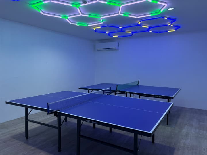 青と緑の六角形のネオンライトが天井を彩る、近未来的なデザインの卓球ルーム。室内には本格的な卓球台が2台設置されており、空調も完備された快適なアクティビティ空間。