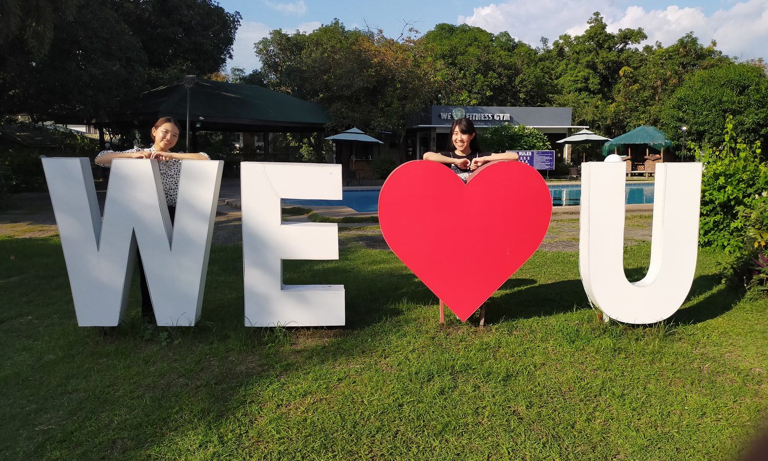 CLARK WE ACADEMYの「WE♥U」のサインの前に立つ留学生