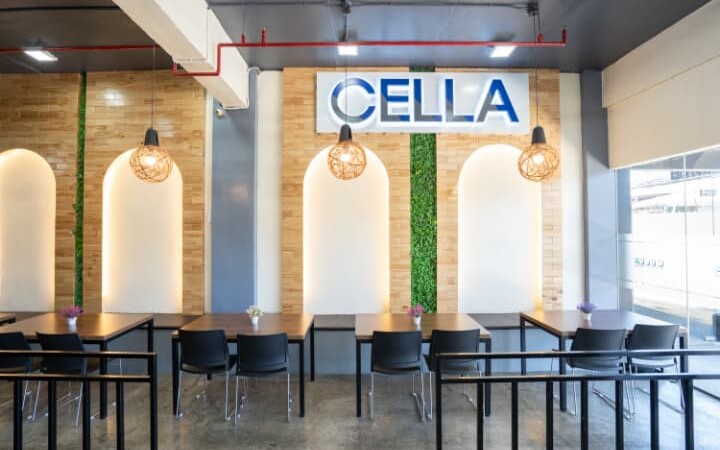 CELLA語学学校の学生ラウンジエリア。木目とグリーンを取り入れたモダンな内装で、壁面にはCELLAのロゴサインが設置されている。学習や休憩にも適した落ち着いたスペース