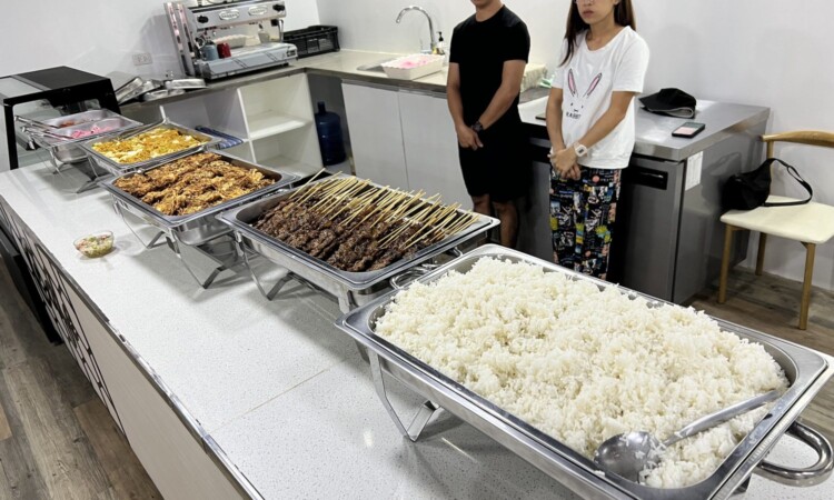 PIAの食堂の配膳カウンター。ご飯とおかずのバットが並び、留学生が取り分けている